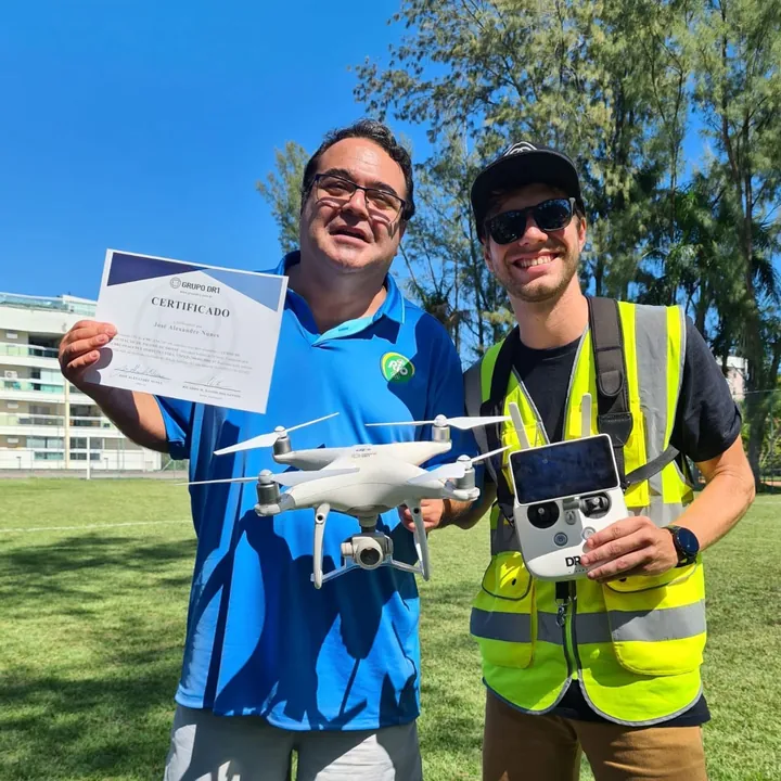 Aluno certificado ao lado de instrutor da DR1 Academy com drone e controle profissional